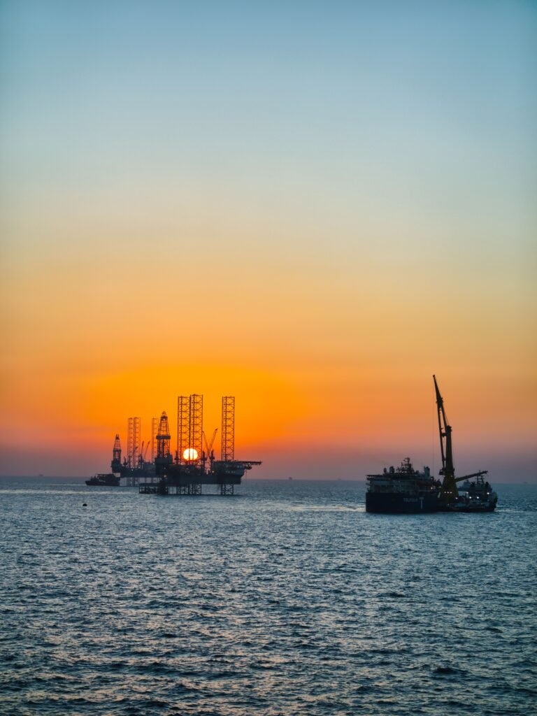 A serene view of an offshore drilling rig and ship at sunset over the ocean.